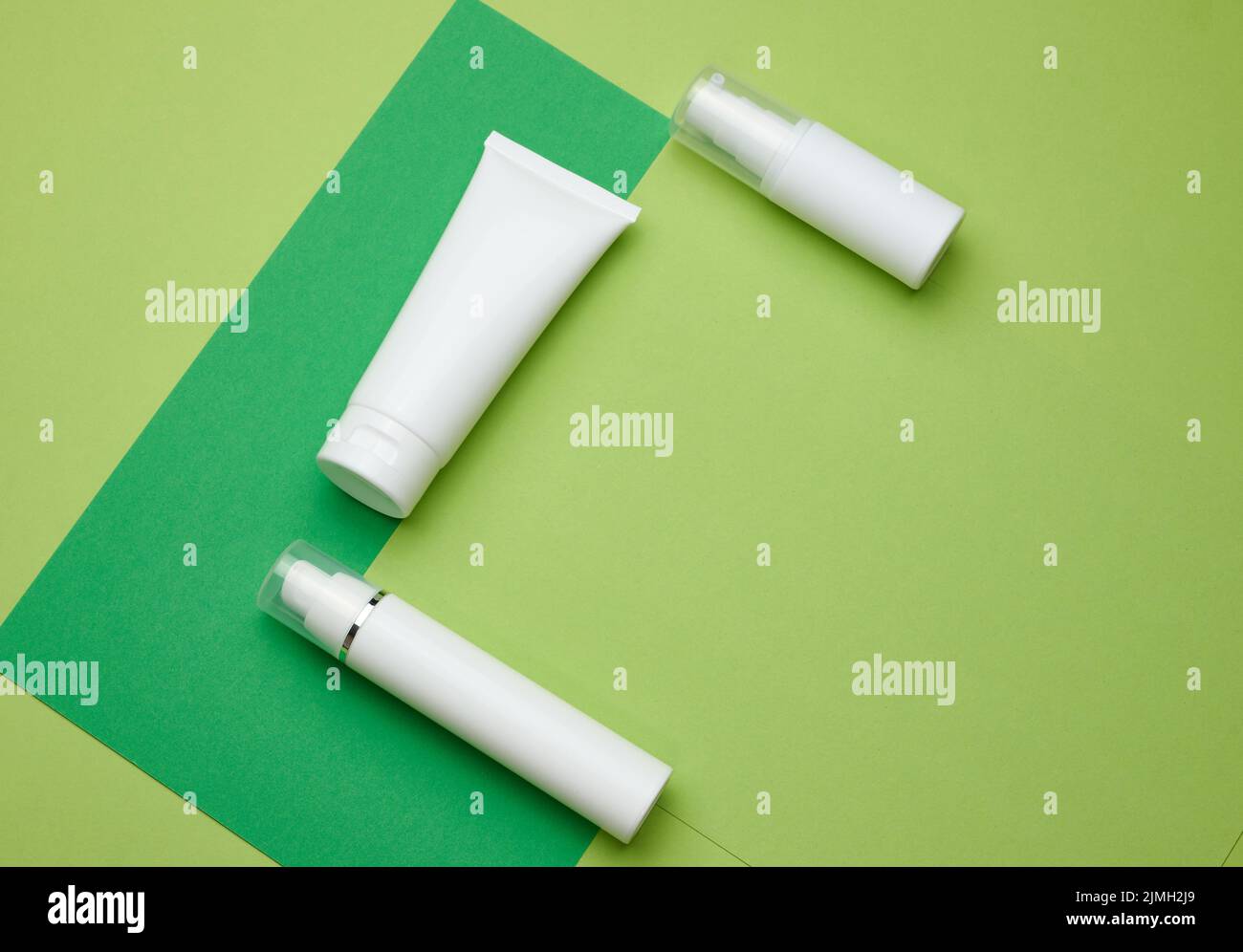 Flacone e tubi bianchi vuoti in plastica per cosmetici su fondo verde. Confezione per crema, gel, siero Foto Stock