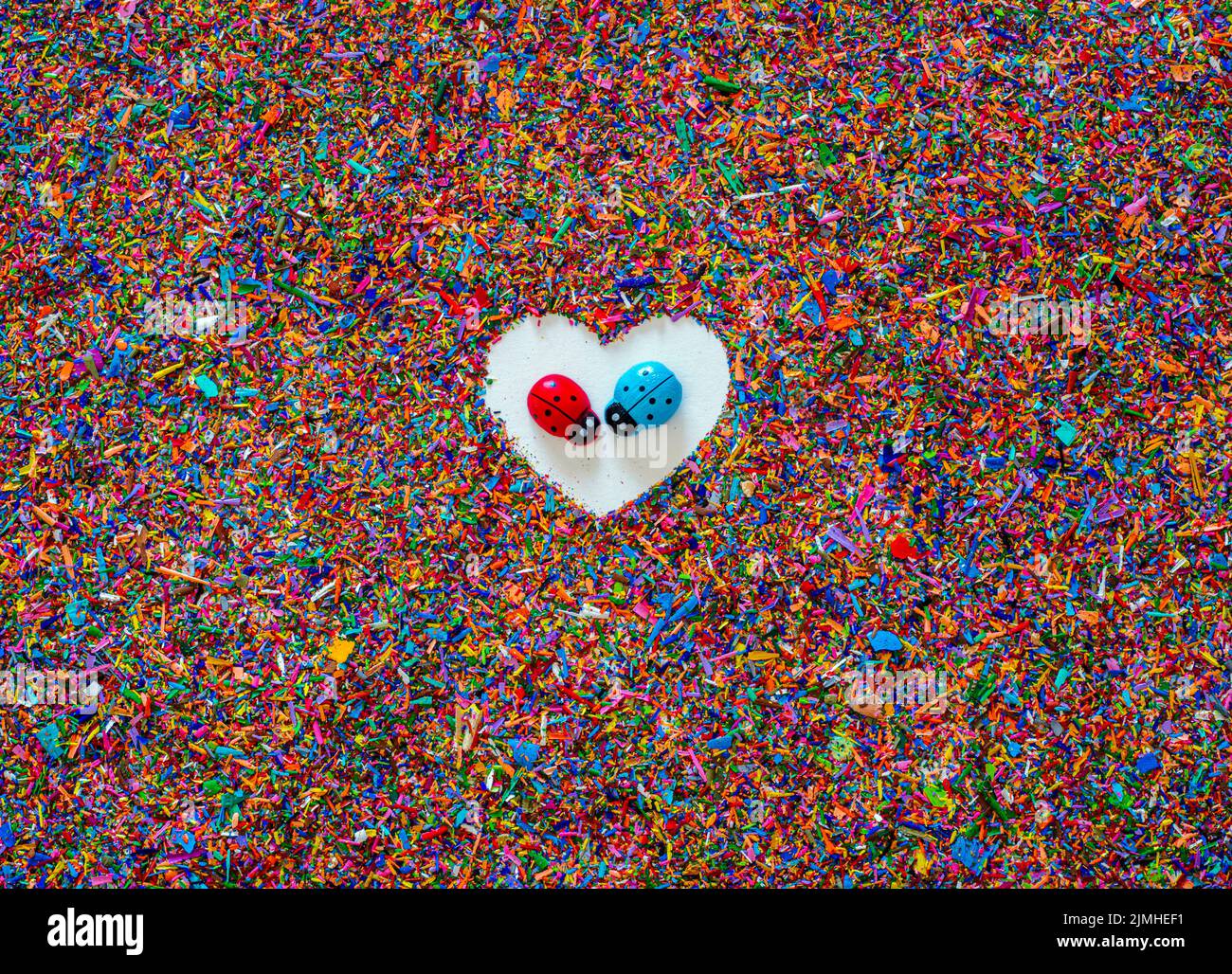 Sfondo testurizzato di scaglie di pastello colorate con un cuore bianco al centro e, al centro di esso, due ladybugs faccia a faccia con amore Foto Stock