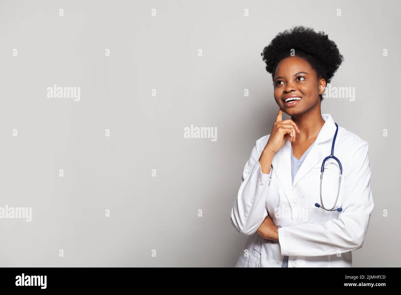 Felice sorridente medico femminile guardando in su su su sfondo bianco della parete dello studio Foto Stock