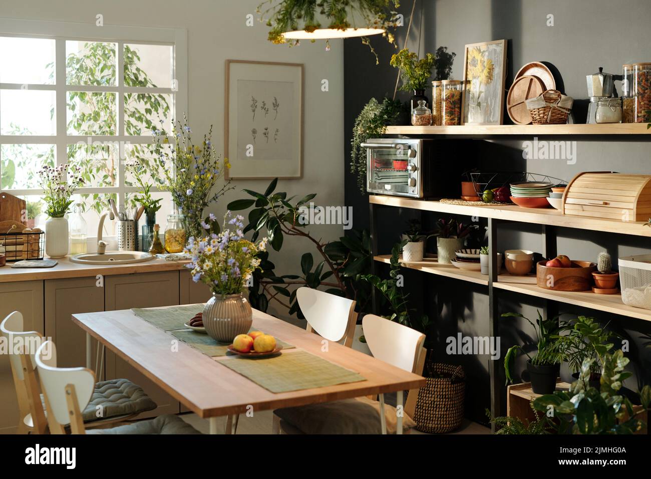 Interno di cucina accogliente con sedie che circondano tavolo con tovaglioli, fiori selvatici in vaso e mele su piatto in piedi dalla finestra Foto Stock