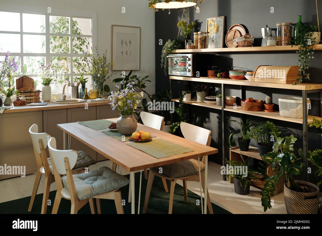 Parte di spaziosa e accogliente cucina con tavolo sostenibile, utensili da cucina e piante della casa a creare l'atmosfera di relax e di ricarica Foto Stock