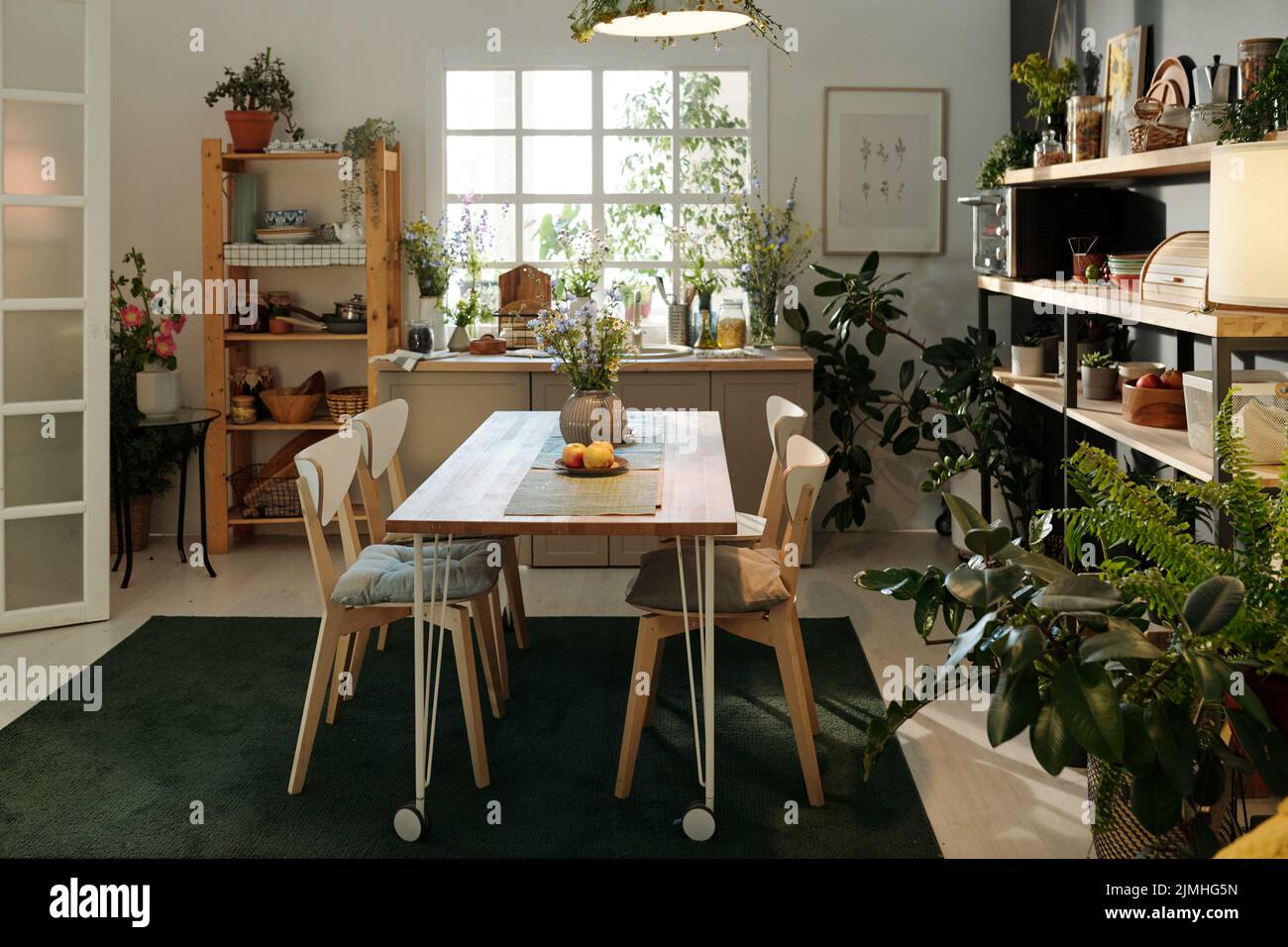 Interno di accogliente cucina in moderno appartamento con tavolo e sedie su tappeto verde scuro circondato da piante domestiche in vasi di fiori Foto Stock