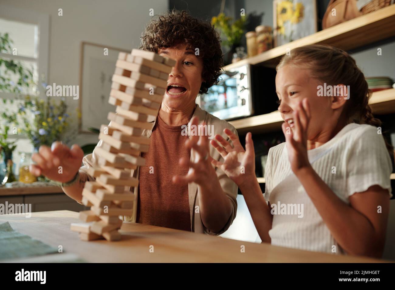Giovane donna e sua figlia giovane cercando di tenere su torre caduto costruito di blocchi di legno mentre si siede da tavolo durante la partita Foto Stock