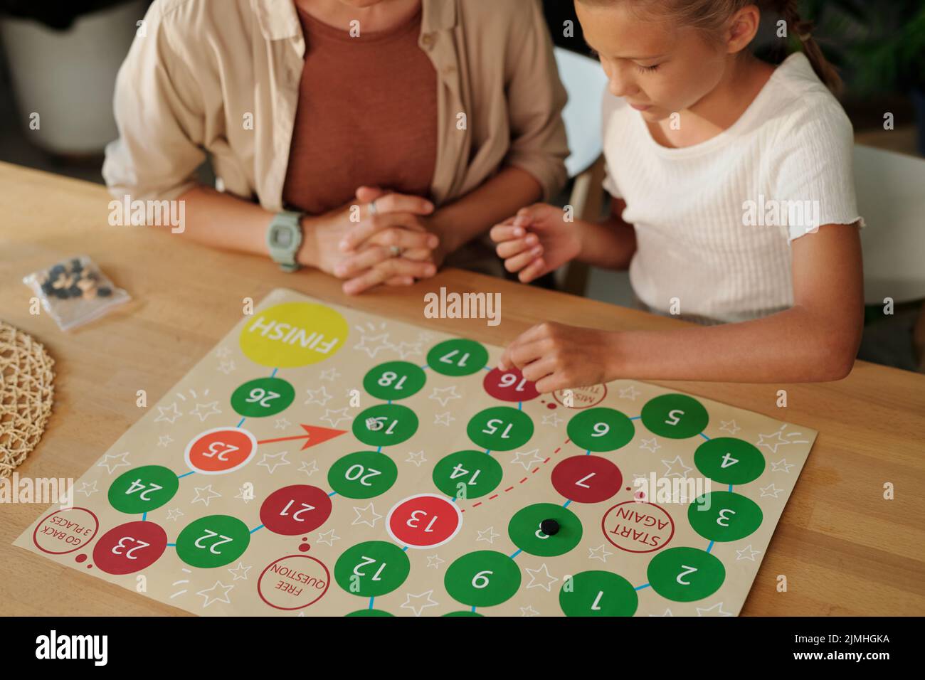 Ragazza giovane in t-shirt che muove chip con carta con cerchi multicolore mentre gioca a bordo con sua madre da tavolo Foto Stock