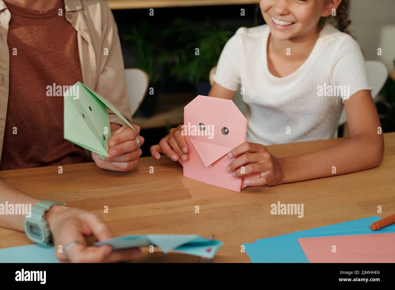 Mani di giovane donna e ragazza felice giovane con animali origami fatti a mano seduti al tavolo e fare giocattoli di carta a piacere Foto Stock