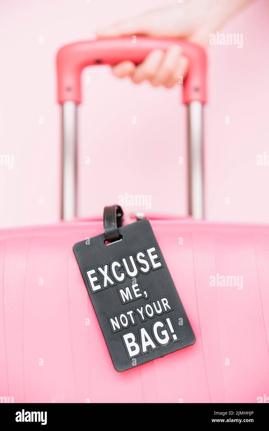 Valigia da viaggio con maniglia per la mano della persona con l'etichetta della borsa su sfondo rosa Foto Stock