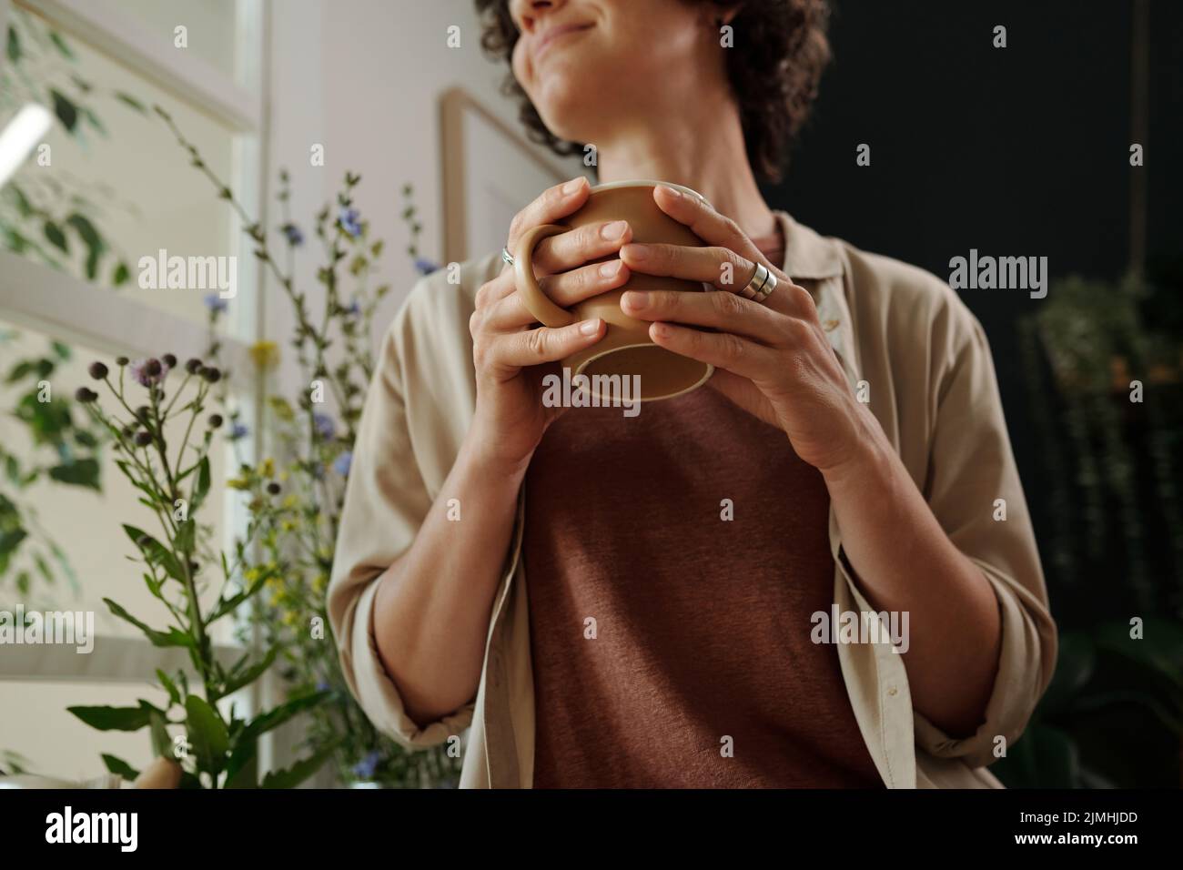 Le mani di giovane donna serena in casa indossano una tazza di tè mentre si fa colazione al mattino in ambiente domestico Foto Stock