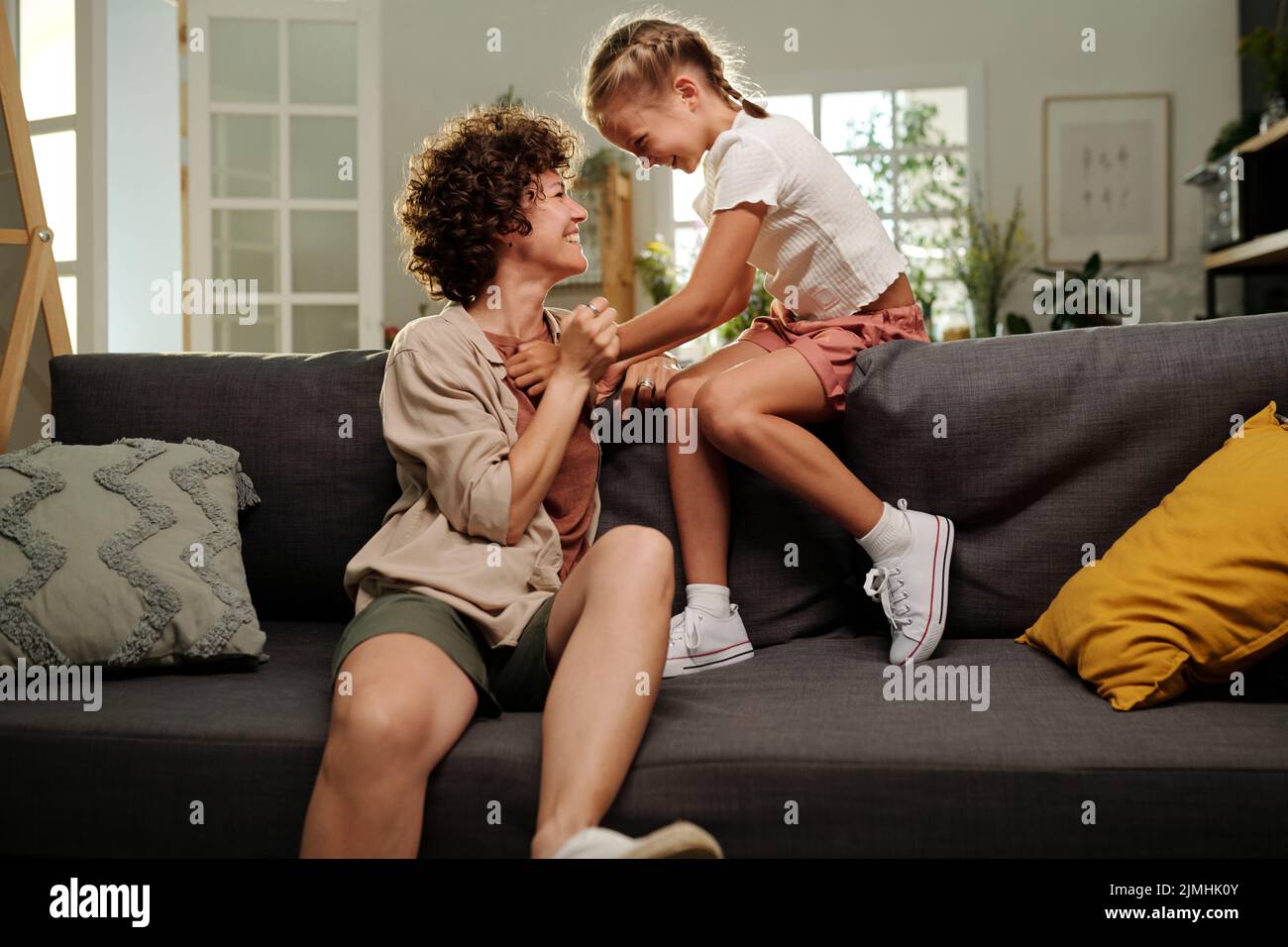 Ragazza allegra carina e la sua madre felice ridendo a qualcosa di divertente mentre si rilassano sul divano e si guardano a vicenda a piacere Foto Stock