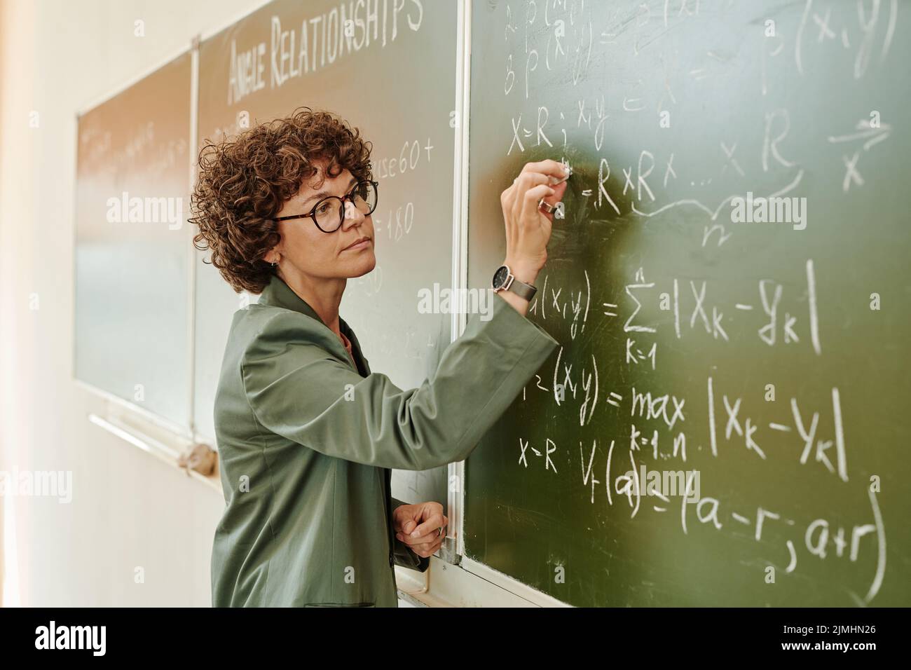 Seria insegnante femminile di algebra con pezzo di gesso che scrive le equazioni sulla lavagna mentre spiega il nuovo soggetto Foto Stock