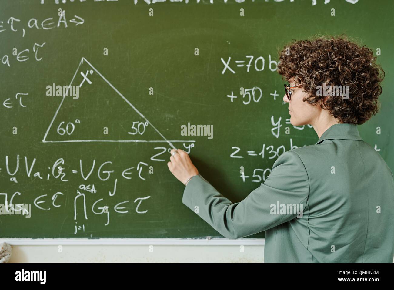 Giovane insegnante serio di università o università che drwing triangolo su lavagna mentre spiega il teorema al pubblico Foto Stock