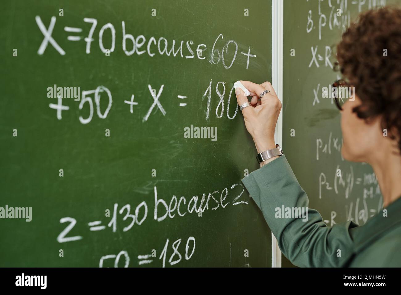 Giovane insegnante del college che scrive l'equazione sulla lavagna a lezione mentre si prepara per la spiegazione del nuovo soggetto agli allievi Foto Stock