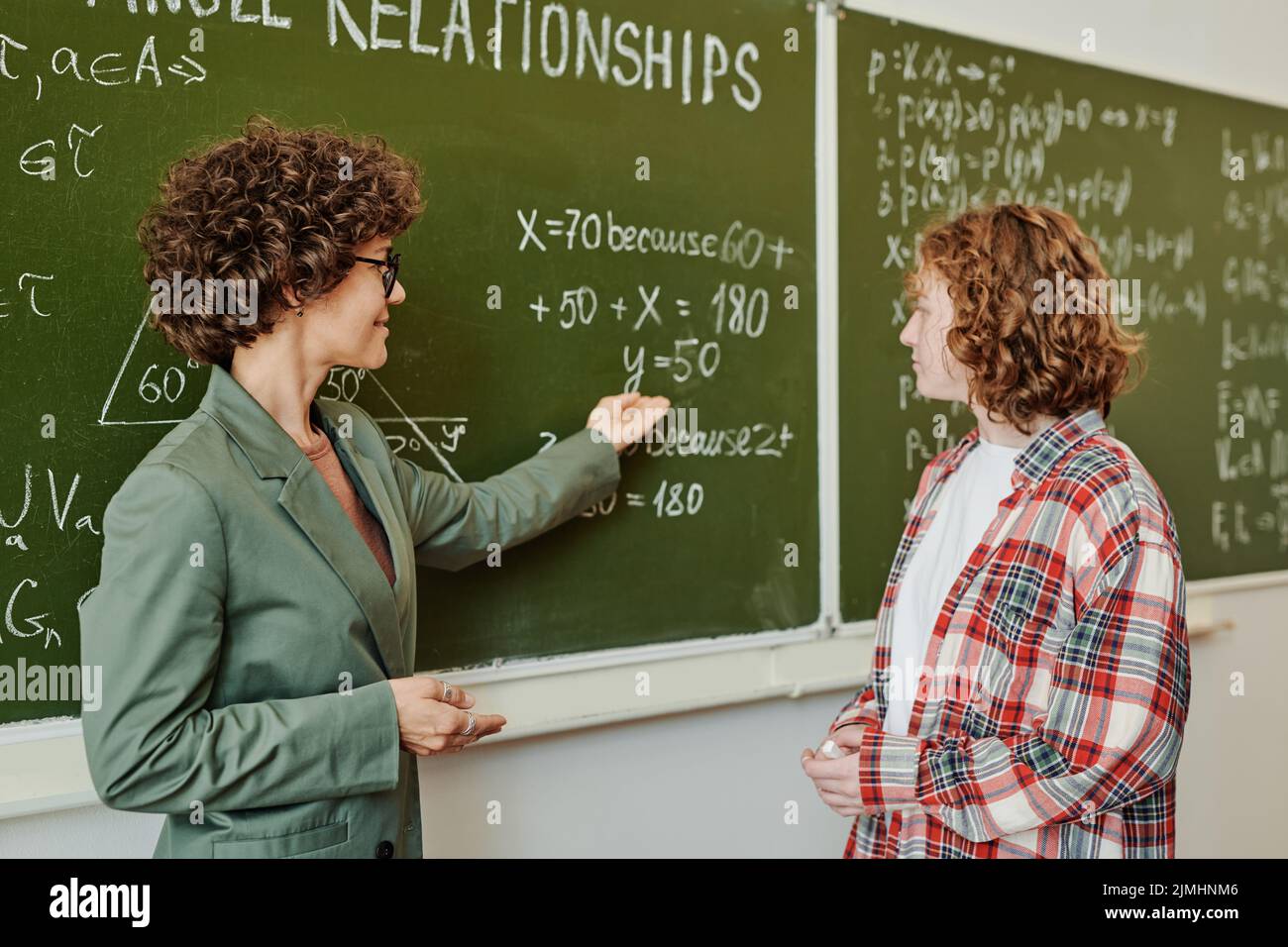 Insegnante fiducioso che spiega la studentessa femminile come risolvere le equazioni e guardarla mentre punta alla lavagna dopo la lezione Foto Stock