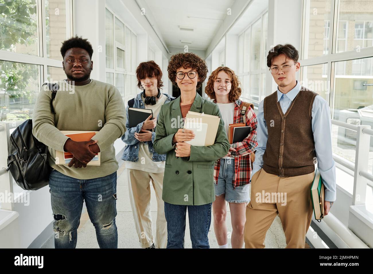 Buon insegnante giovane e allegro studenti teenage multiculturale in casualwear in piedi nel corridoio del college o dell'università Foto Stock