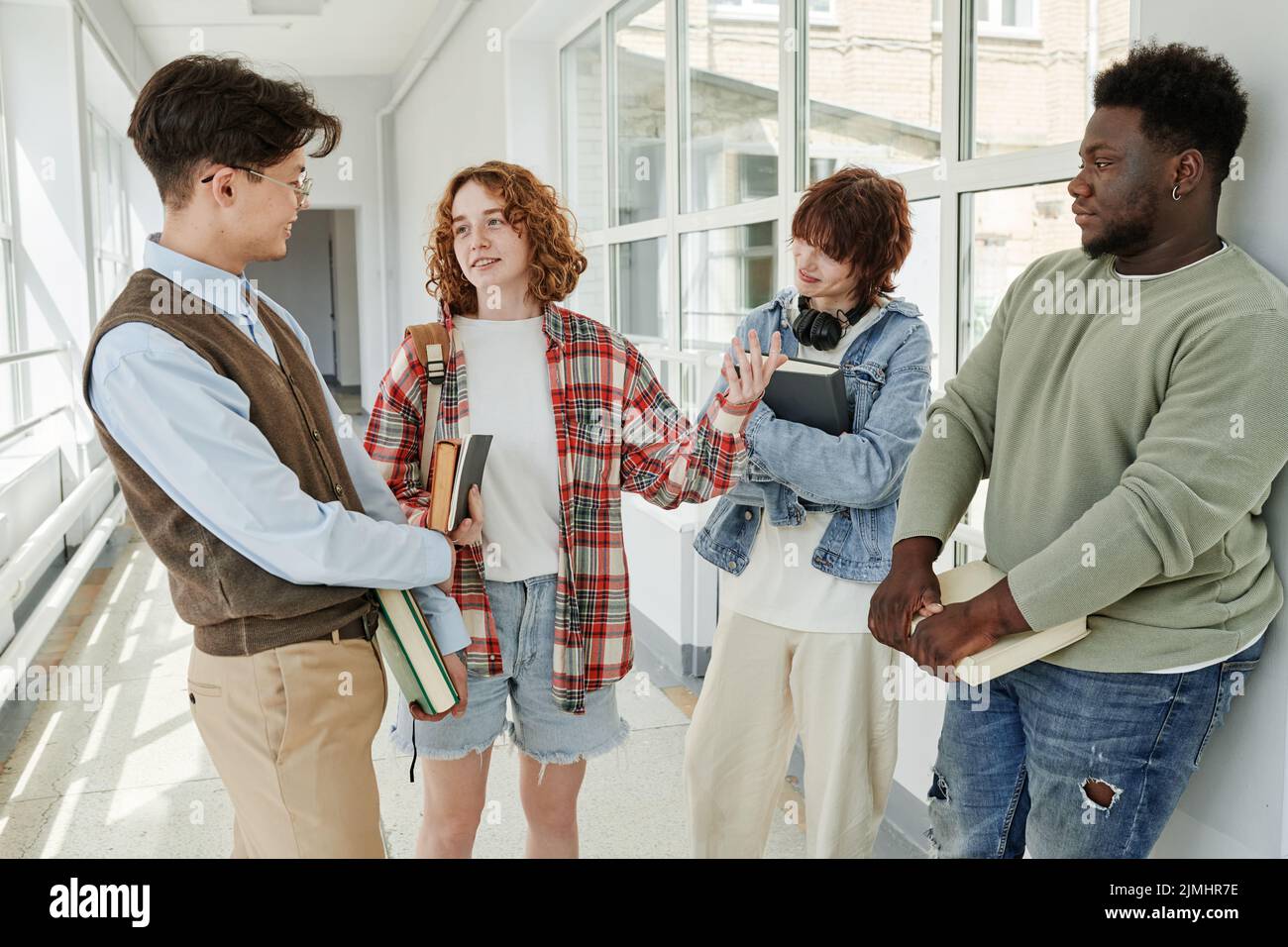 Ragazza adolescente felice che guarda il tipo asiatico durante la discussione della storia della letteratura o libro con i compagni di classe nel corridoio dell'università dopo le lezioni Foto Stock