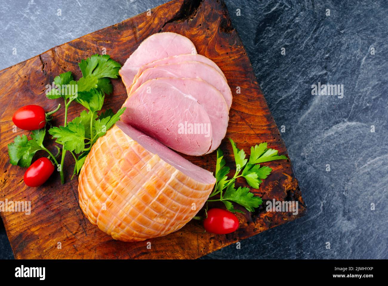 Tradizionale prosciutto di Pasqua tedesco bollito con pomodori e prezzemolo offerto come vista dall'alto su un vecchio rustico bordo di legno con spazio copia Foto Stock