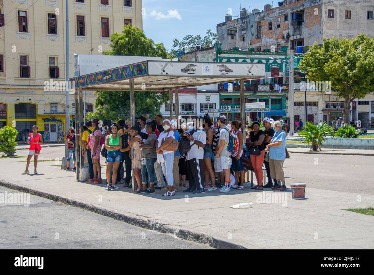 Un gruppo di persone affollate sotto la tettoia, in attesa di un autobus per arrivare. L'Avana, Cuba. Foto Stock