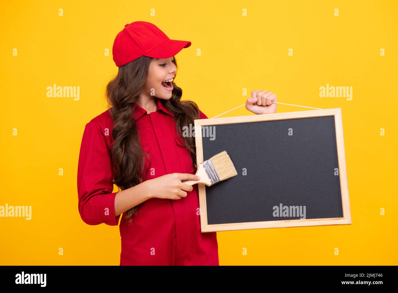 Felice ragazza sorridente costruttore nella costruzione uniforme e cappello. Pittore con pennello o rullo per pittura. Il lavoratore tiene la lavagna isolata su Foto Stock