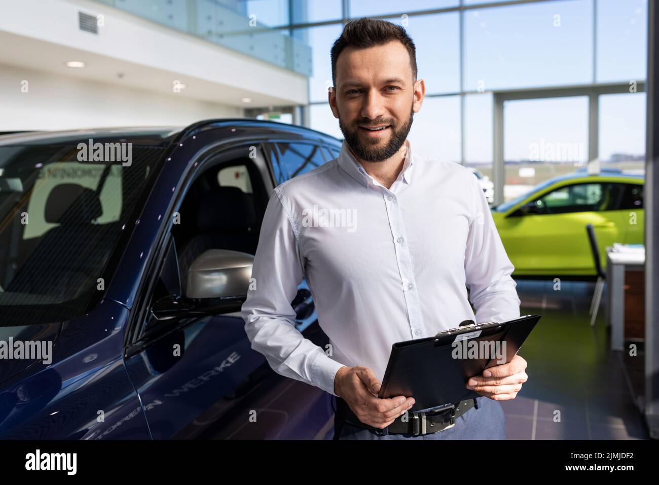 Affascinante venditore in una concessionaria di auto sullo sfondo di nuove auto premium Foto Stock