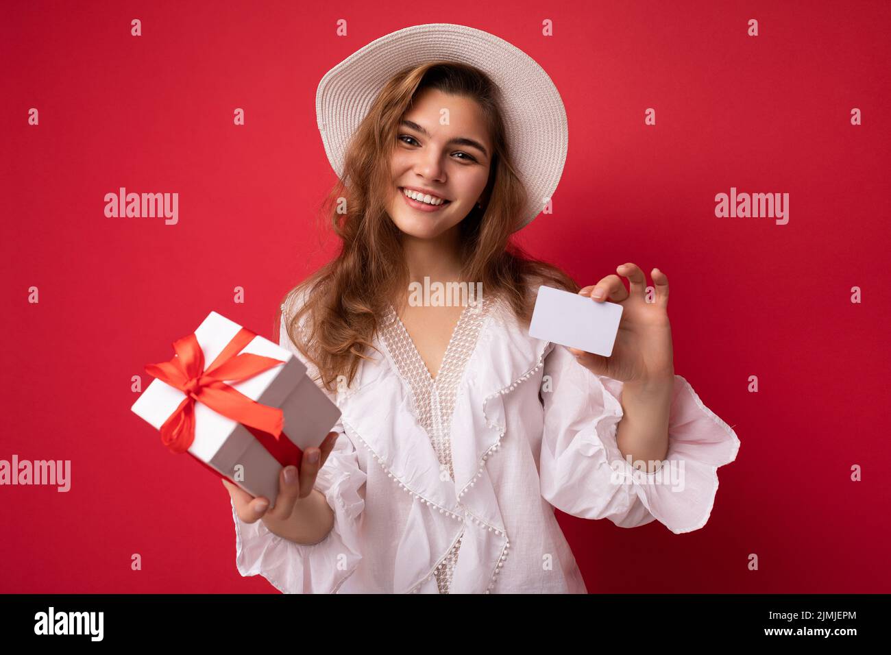 Ritratto di donna allegra positiva alla moda in formalwear con scatola regalo e carta di credito guardando la macchina fotografica isolato sul rosso Foto Stock