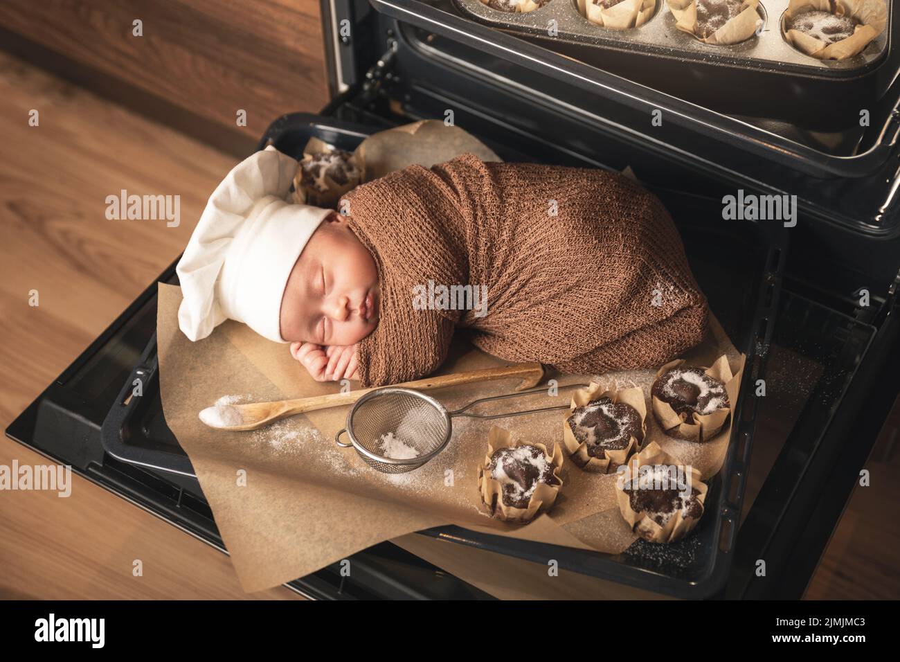 Il neonato che indossa il cappello dello chef si trova sul vassoio del forno con un muffin Foto Stock