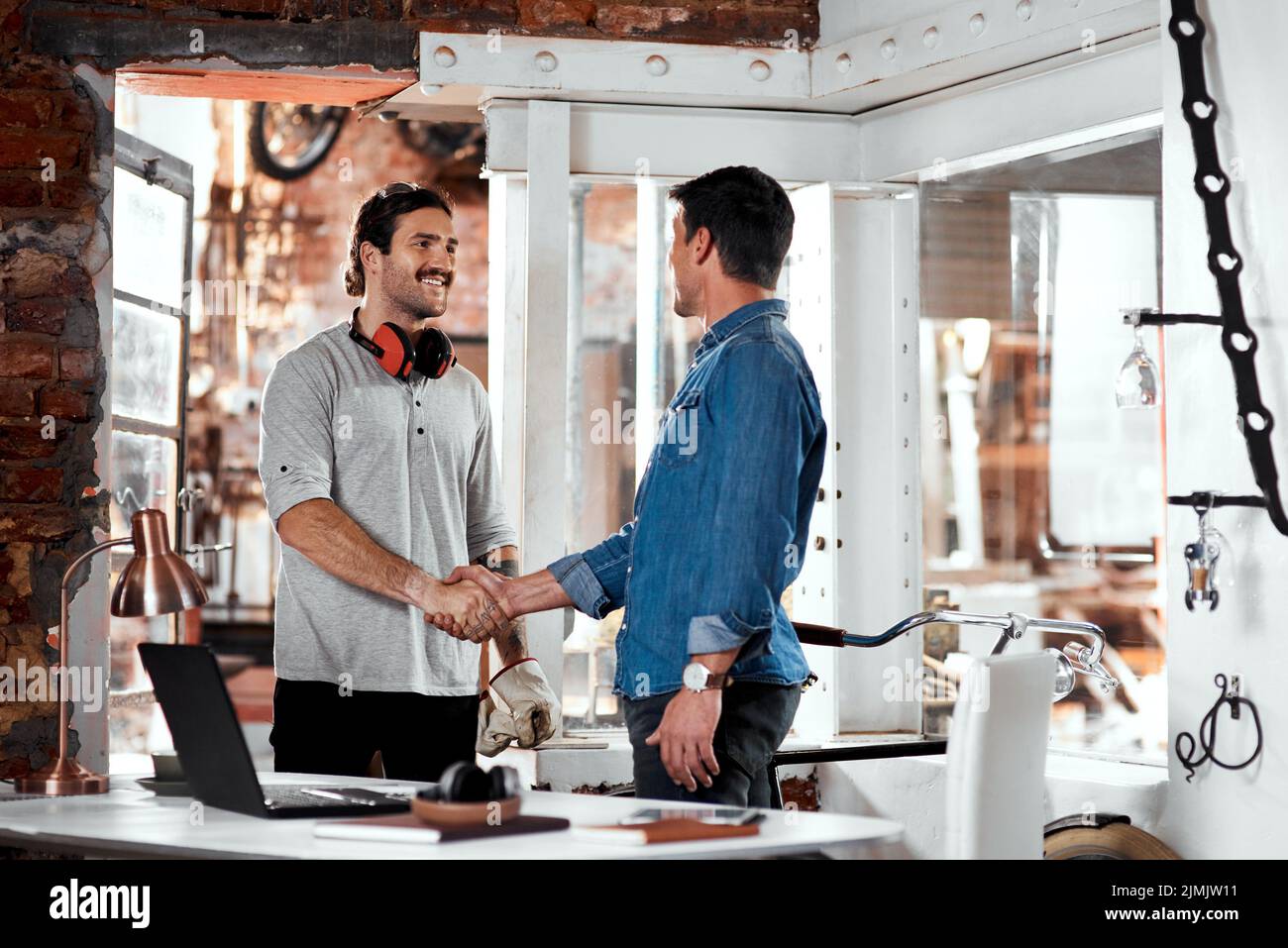 Riunitevi e fate della vostra azienda un successo. Due giovani uomini d'affari che si scuotono le mani in un ufficio all'interno della loro officina. Foto Stock