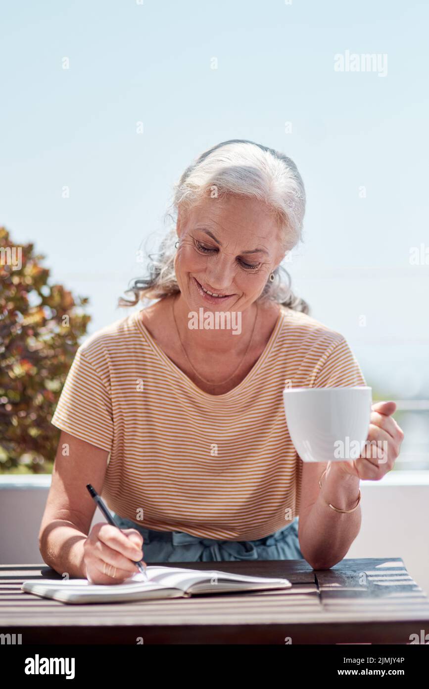 Vivere il tipo di vita i più venduti sono fatti di. Una donna matura che ha il caffè e la scrittura in un taccuino sul balcone a casa. Foto Stock