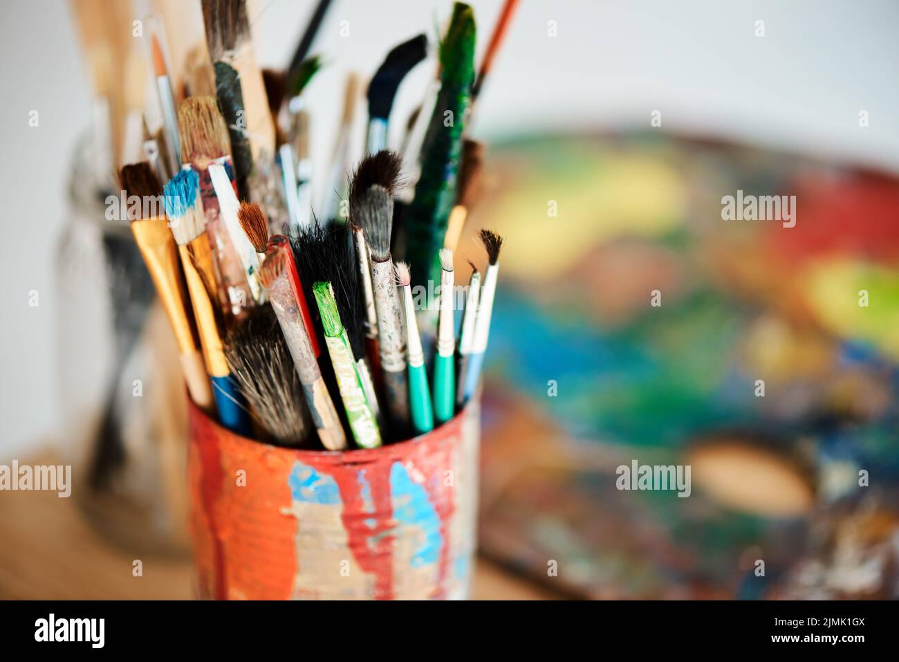 Lets get painting. Una lattina piena di pennelli in uno studio d'arte vuoto dopo una lezione di pittura. Foto Stock