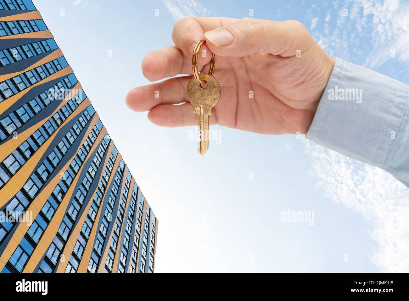 Chiave di appartamento in mano di un uomo. Chiave di bloccaggio porta in ottone. Edificio moderno contro il cielo blu. Vista dal basso. Foto Stock