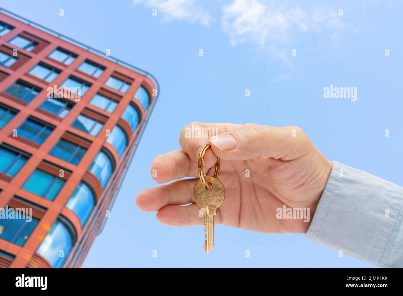 La chiave dell'appartamento in una mano dell'uomo. Chiave per serratura in ottone. Edificio moderno con vista dal basso. Architettura nella città moderna. Vendita di un Foto Stock