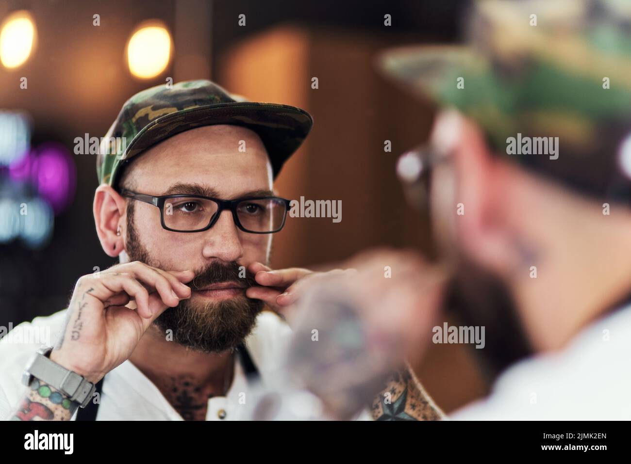 Controllo della barba. Un bel giovane che guarda nello specchio ed esamina la barba all'interno di un barbiere. Foto Stock