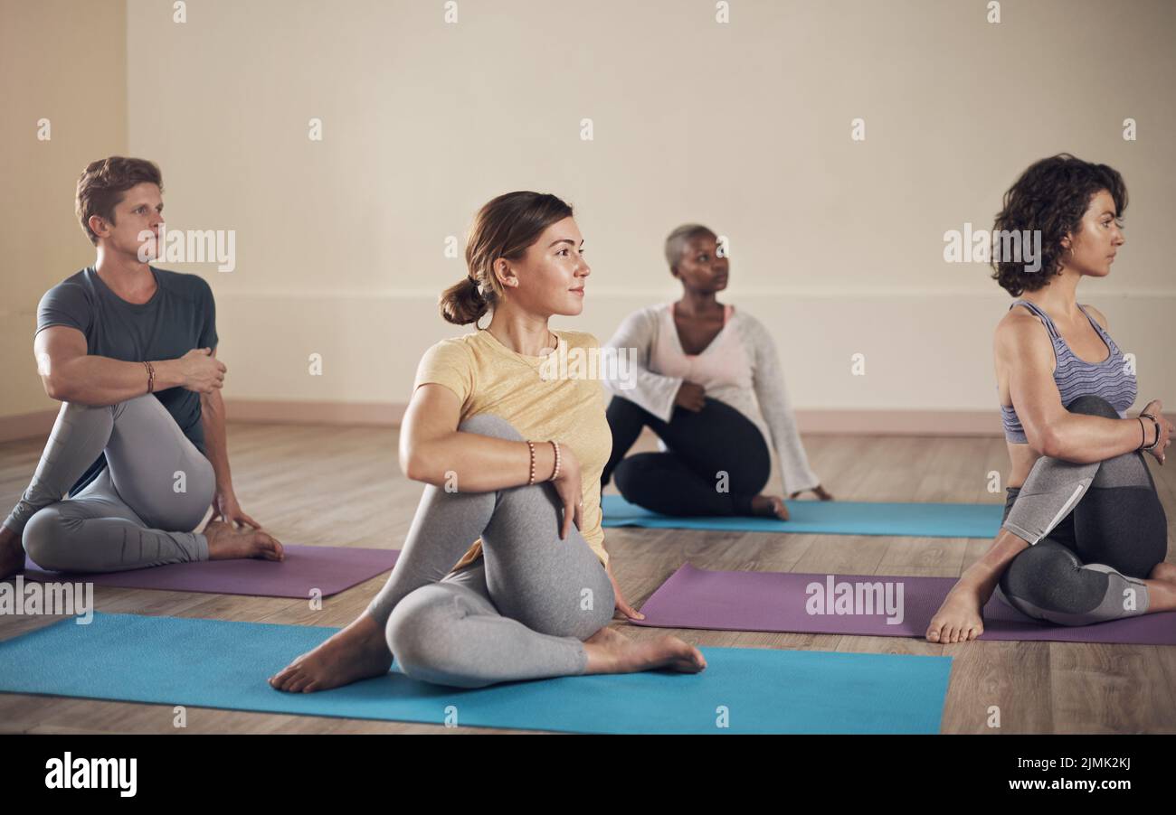 Rilasciando la tensione dalla spina dorsale. Shot completo di un gruppo diversificato di yoga che tiene in posa una mezza torsione spinale durante una sessione interna di yoga. Foto Stock