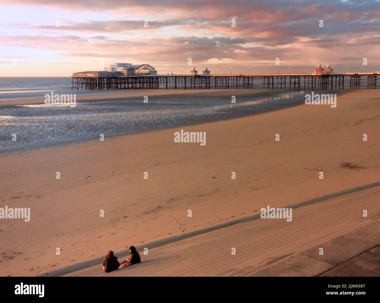 Due donne che guardano il tramonto sullo storico molo nord di blackpool con la luce brillante riflessa sulla spiaggia e colou Foto Stock