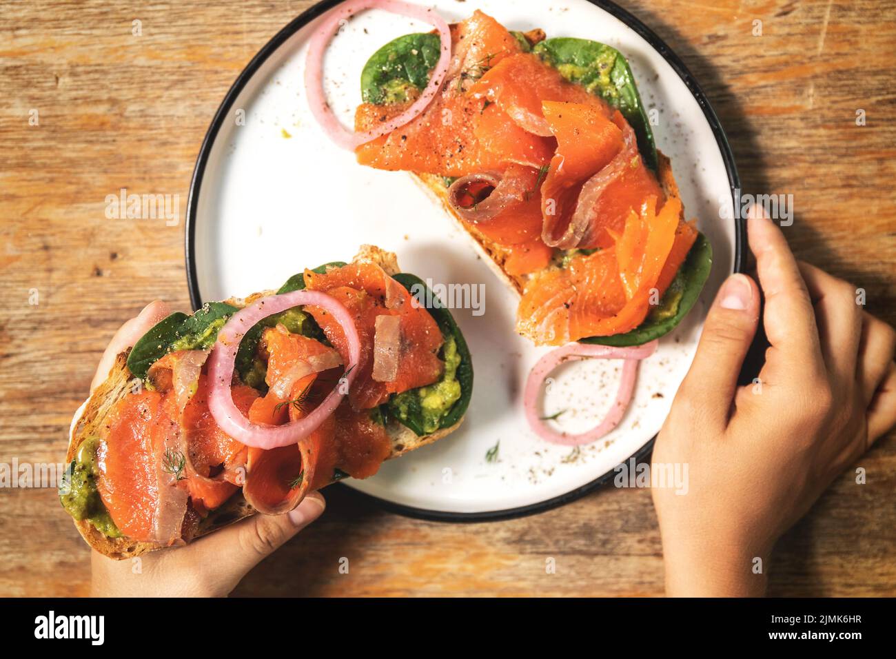 Mani femminili e toast deliziosi con salmone affumicato, avocado e foglie di basilico Foto Stock