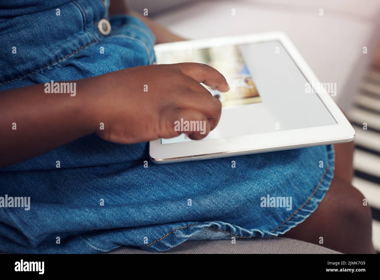 Un solo tocco ti porta in un mondo di avventura: Una bambina irriconoscibile che usa un tablet digitale mentre sei seduto sul divano di casa. Foto Stock