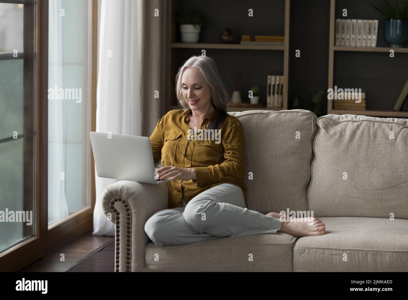 Felice anziano utente laptop donna che riposa su un morbido divano Foto Stock