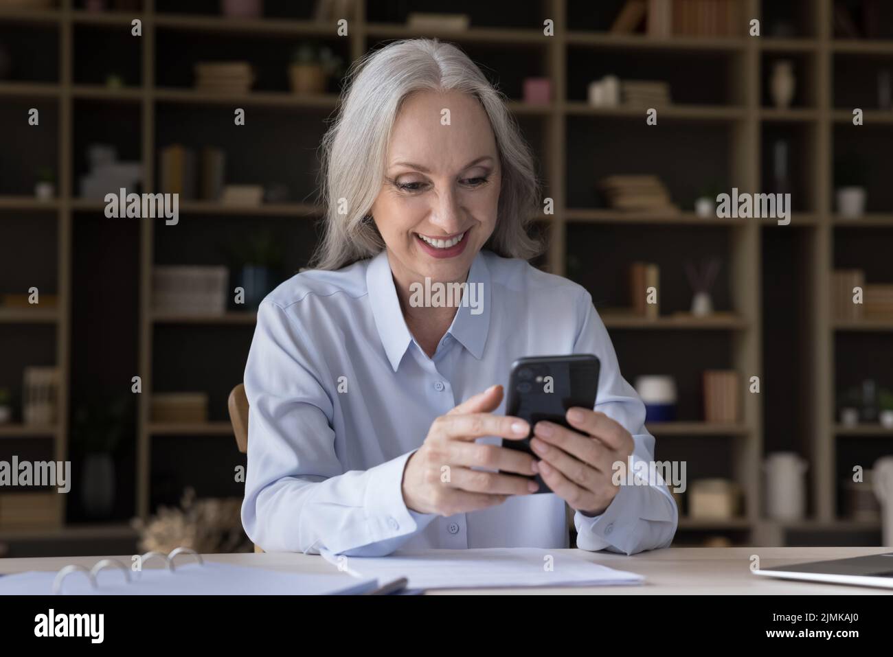 Donna d'affari anziana allegra che usa lo smartphone a casa Foto Stock