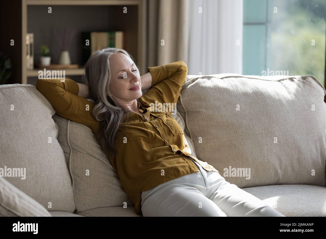 Tranquilla e sonnolenta anziana donna padrona di casa seduta su un morbido divano Foto Stock