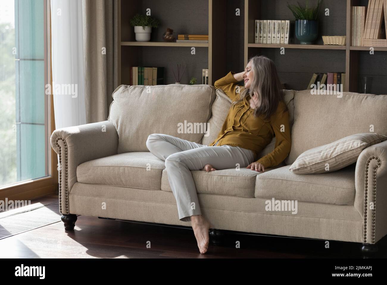 Felice bella donna anziana grigia con capelli seduti su un comodo divano Foto Stock