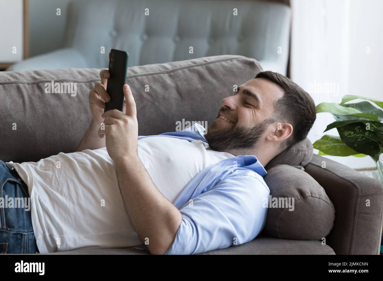 Uomo singolo sdraiato sul divano con smartphone Foto Stock