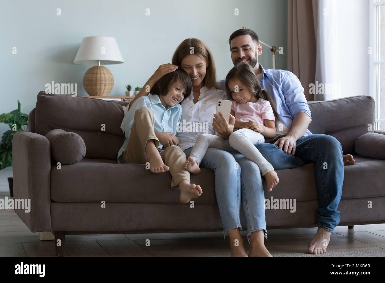 Coppia con i bambini piccoli si siedono sul divano usando il cellulare Foto Stock