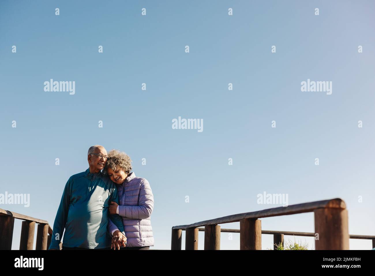Amorevole coppia anziana sorridendo e tenendo le mani mentre si cammina lungo un ponte pedonale sul mare. Coppia anziana affettuosa che gode di una spiaggia rilassante Foto Stock