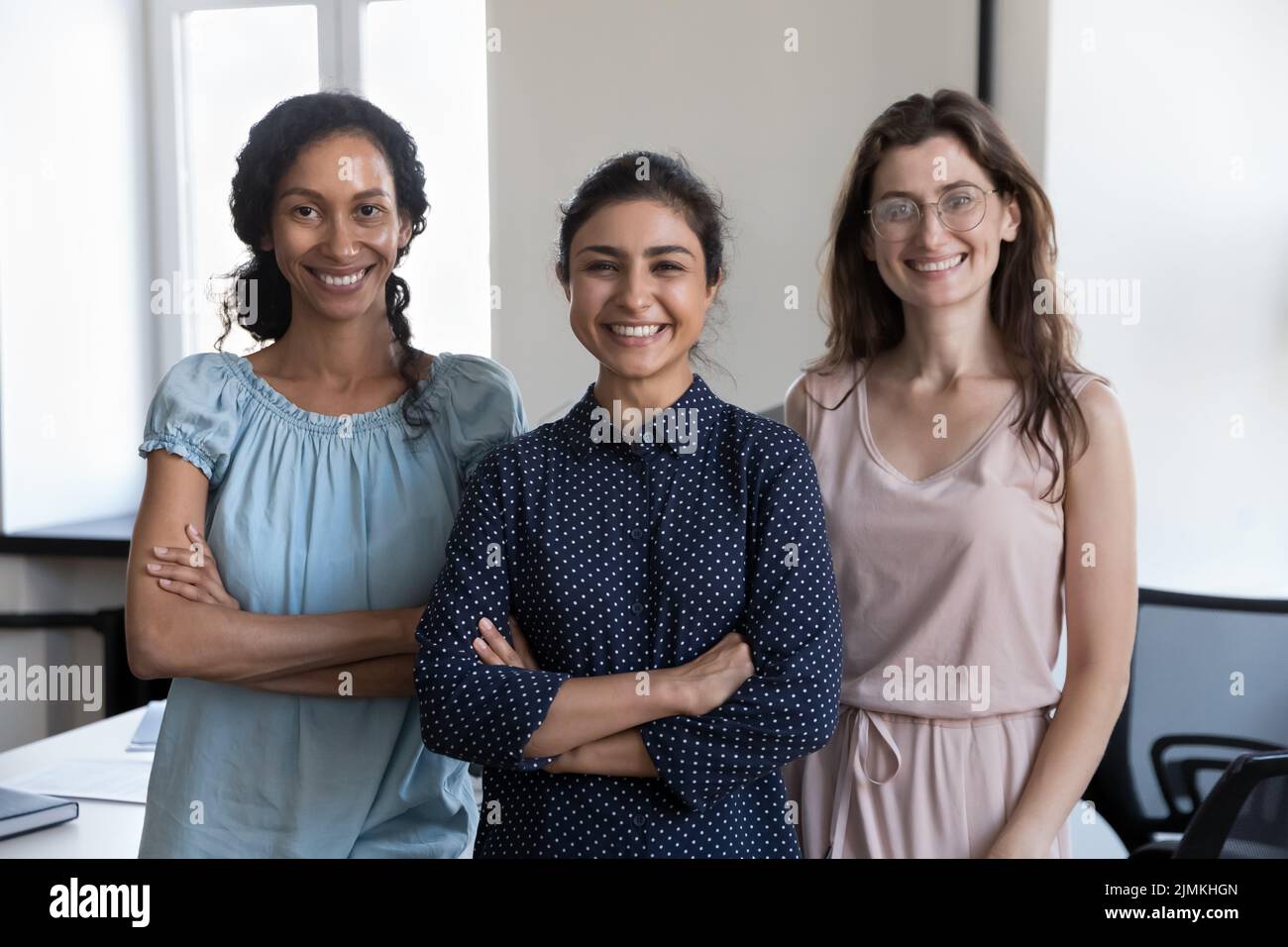 Tre donne d'affari multietniche posano sul posto di lavoro sorridendo fissando la macchina fotografica Foto Stock