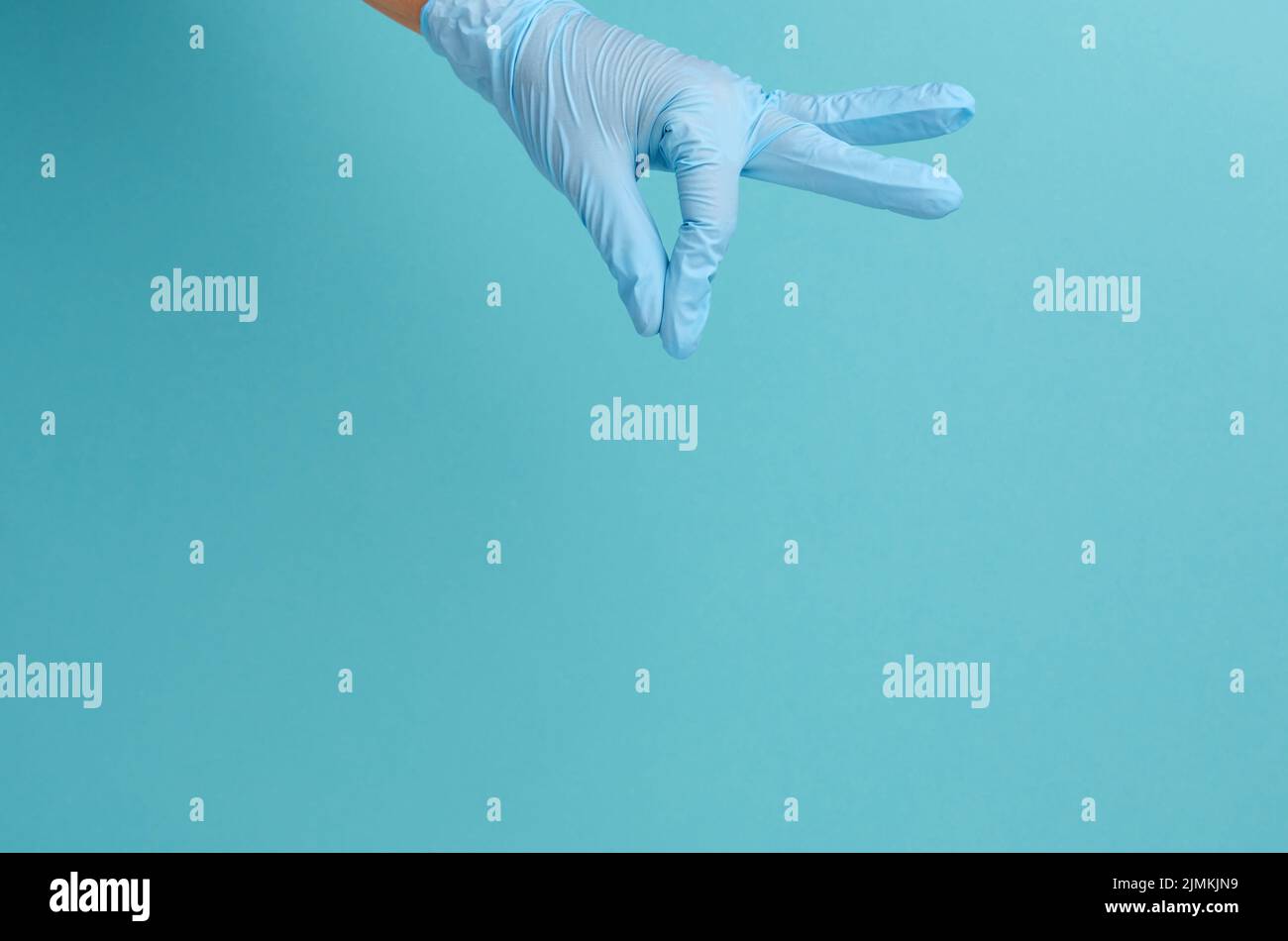 La mano del medico in un guanto medico blu tiene un oggetto su uno sfondo blu Foto Stock
