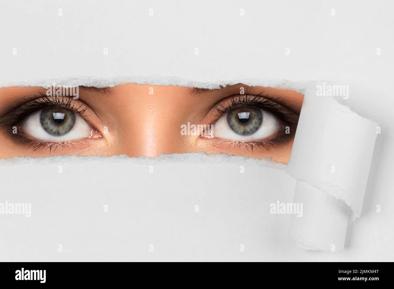 Occhi femminili giovani che guardano attraverso la carta strappata Foto Stock