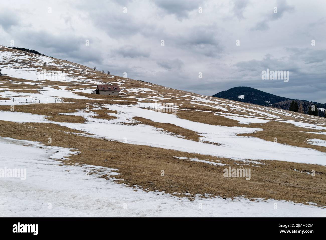 Un ripido prato alpino coperto di neve con una piccola capanna. Il cielo è pieno di nubi scure di tempesta di tuoni e testimonia un'imminente tempesta di neve. Foto Stock