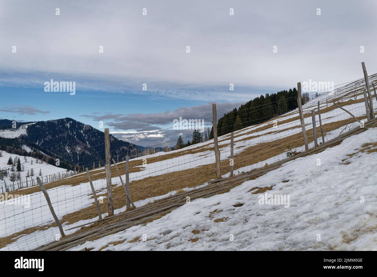 Un ripido prato alpino coperto di neve con una recinzione in legno. Il cielo blu profondo è parzialmente coperto e annuncia la prossima tempesta di neve. Foto Stock