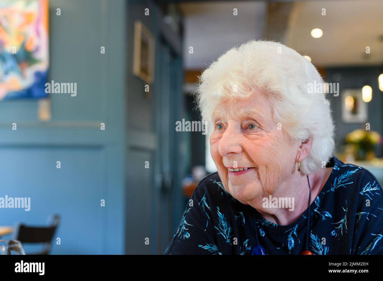 Una donna caucasica anziana sorridente con capelli bianchi seduti in un bar Foto Stock