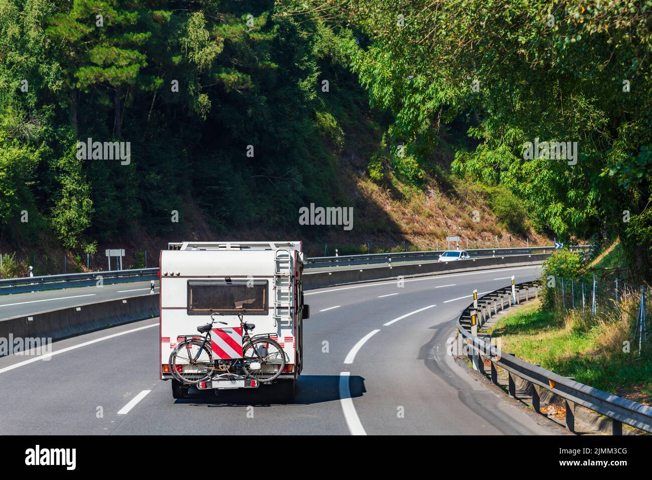 Motorhome con una bicicletta dietro guida su una strada circondata da alberi Foto Stock