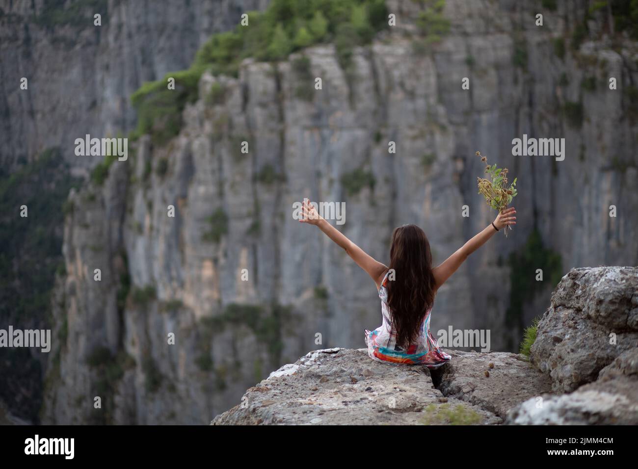 La giovane ragazza con i fiori in mano, che ha fatto un segno di vittoria mentre guardava la vista del canyon. Foto Stock