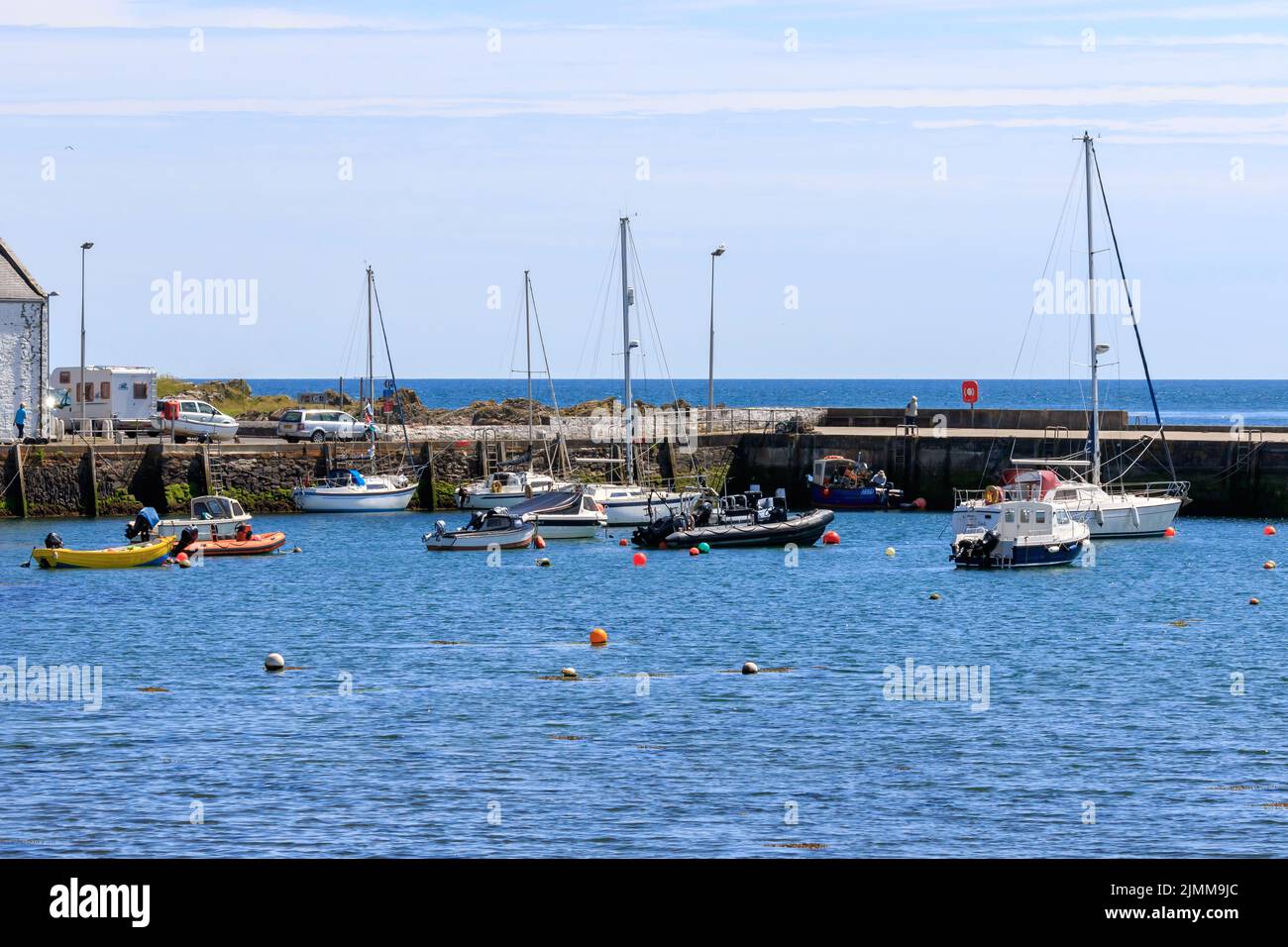 The , Isola di Whithorn, Scozia - 15 giugno 2022: Barche a vela illuminate dal sole e gommoni ormeggiati nel porto Foto Stock